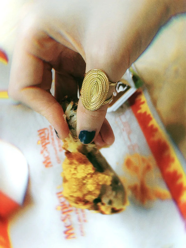 Fairies Whisper Friday Shield Ring worn on hand holding fried chicken, bold warrior-inspired jewelry styling