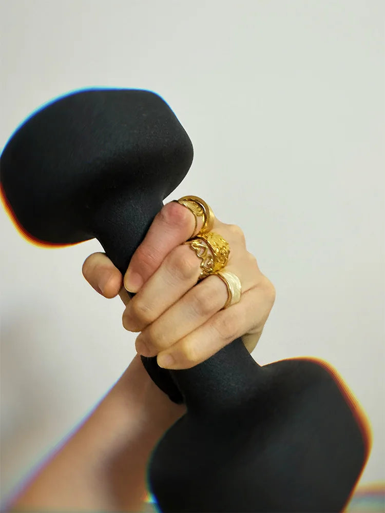 Fairies Whisper Venus de Milo Ring worn with multiple rings while holding black dumbbell, gold jewelry symbolizing strength through imperfection