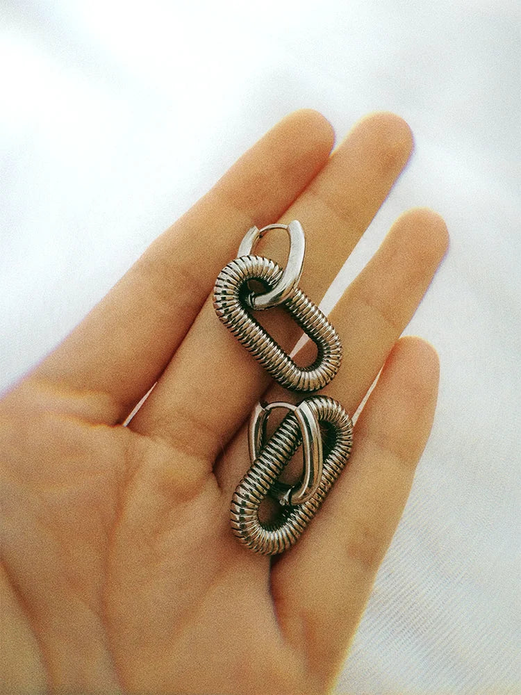 Silver Arena hoop earrings displayed on hand, width about two fingers for size reference.