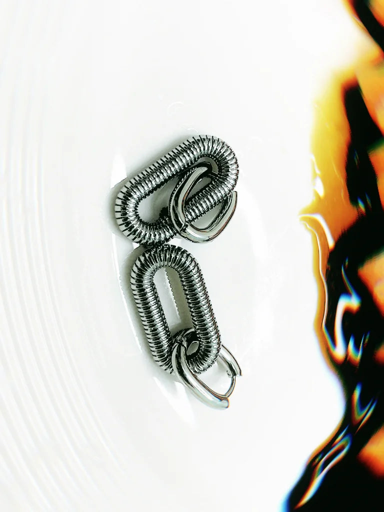 Silver spiral Arena earrings, oval spring-like structure with industrial and ancient architectural design.